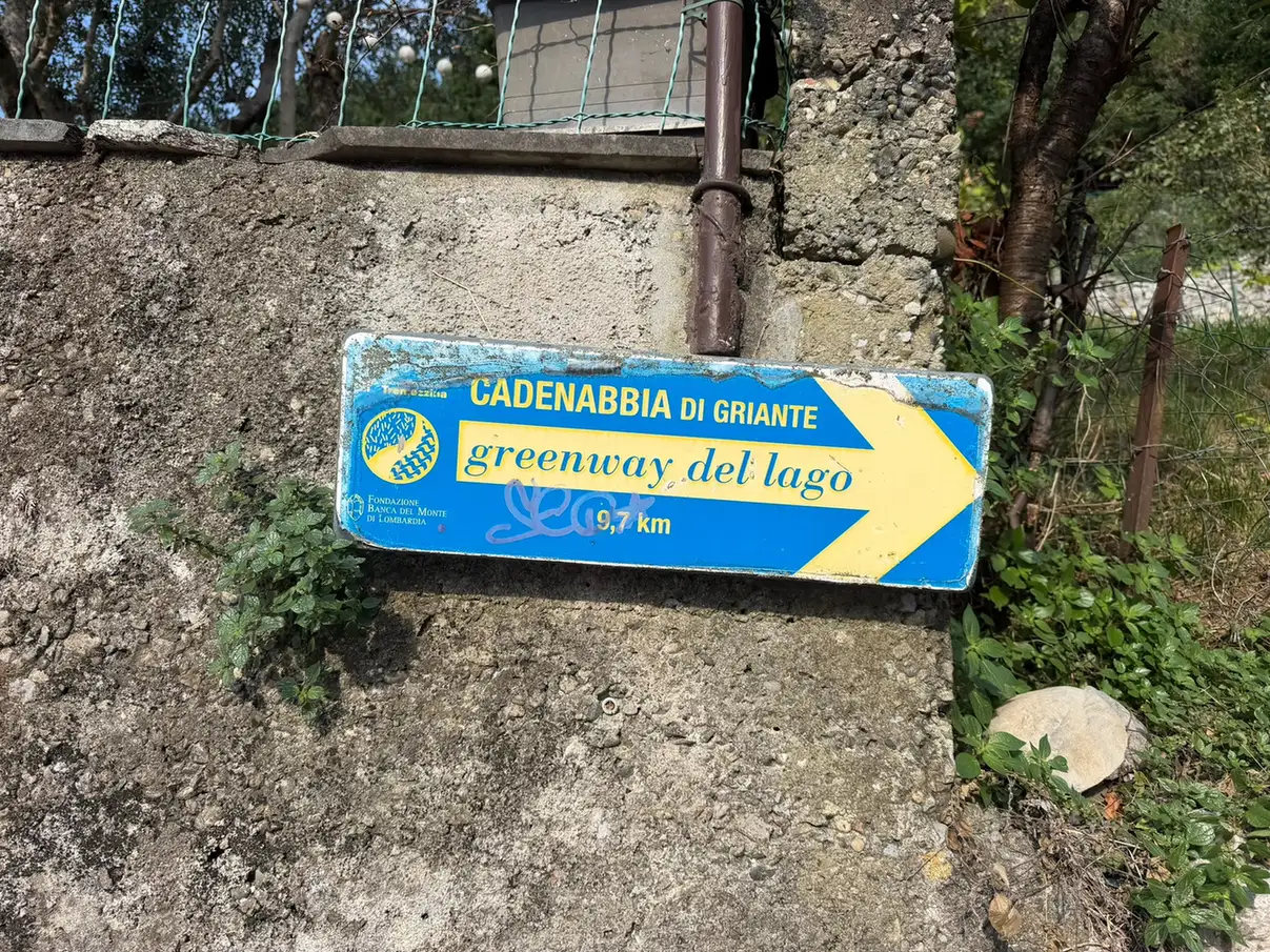 Żółty znak Greenway del Lago na kamiennym murze